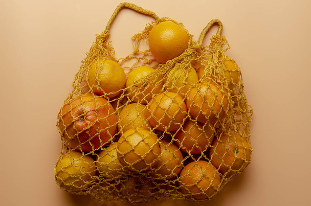Mesh bag of fresh oranges healthy citrus fruits from on peach background - Фото, зображення