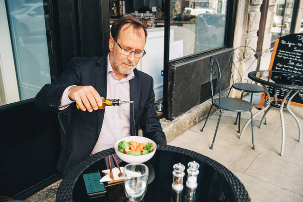 İş adamı dışarıda bir kafede terasta yemek yiyor, takım elbise giyiyor. Somonlu sağlıklı yeşil salata.  - Fotoğraf, Görsel