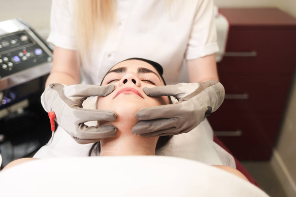 Doctor cosmetologist does facial massage to the patient with electric gloves - Photo, Image