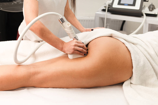 Doutor cosmetologista com um rolo em suas mãos faz uma massagem nádegas com dispositivo closeup - Foto, Imagem