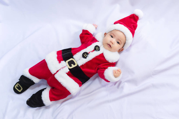 little baby wearing red Santa Claus costume sleep on white fur carpet. Concept of celebrates Christmas and New Year's holidays. - Foto, imagen