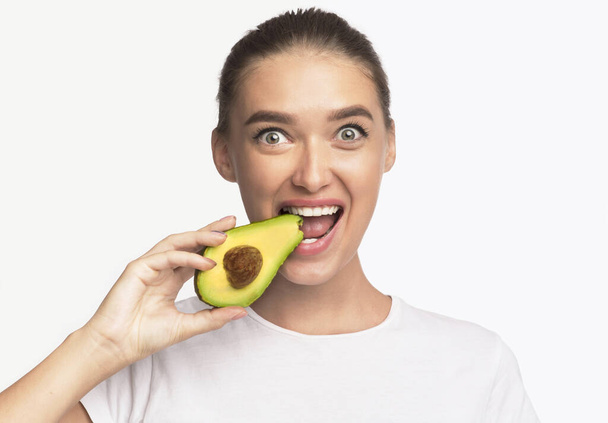 Young Lady Eating Avocado Smiling At Camera Standing, Studio Shot - Foto, afbeelding