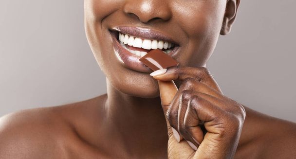 Μαύρο κορίτσι με λευκό υγιή δόντια δαγκώνει σοκολάτα γάλακτος φέτα - Φωτογραφία, εικόνα