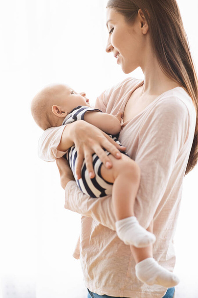 Νεαρή ευτυχισμένη γυναίκα που κρατάει τρυφερά το νεογέννητο μωρό της στην αγκαλιά - Φωτογραφία, εικόνα