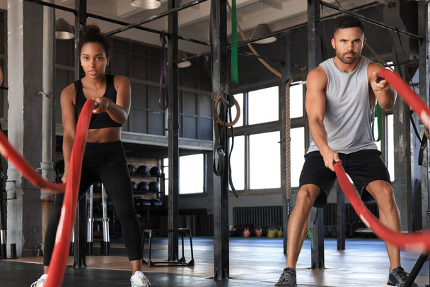 Athletic young couple with battle rope doing exercise in functional training fitness gym. - Foto, afbeelding