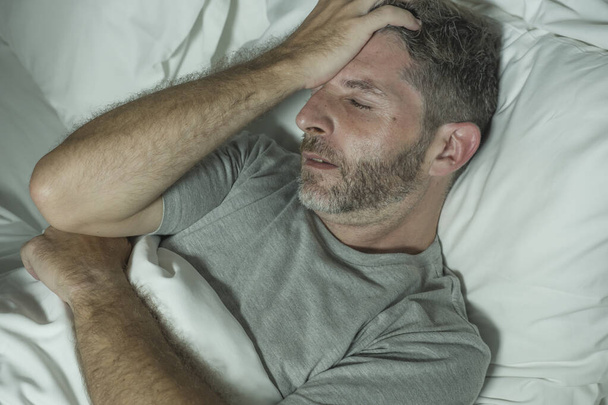 dramatic portrait of stressed and frustrated man in bed awake at night suffering insomnia sleeping disorder tired and desperate unable sleep feeling exhausted  - Fotografie, Obrázek