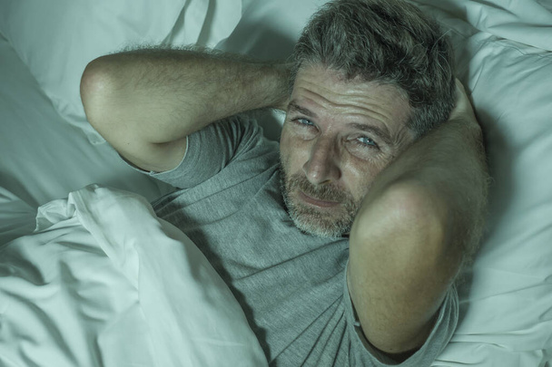 dramatický portrét stresovaného a frustrovaného muže v posteli vzhůru v noci trpí nespavostí poruchy spánku unavený a zoufalý nemůže spát pocit vyčerpanosti  - Fotografie, Obrázek