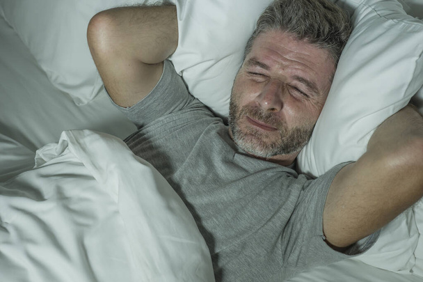 dramatyczny portret zestresowanego i sfrustrowanego mężczyzny w łóżku obudzonego w nocy cierpiącego na bezsenność zaburzenia snu zmęczonego i zdesperowanego niemogącego spać wyczerpanego  - Zdjęcie, obraz