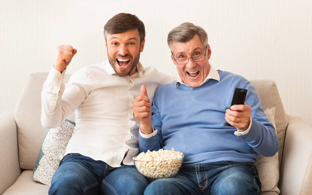 Man And Elderly Father Watching Match On TV At Home - 写真・画像