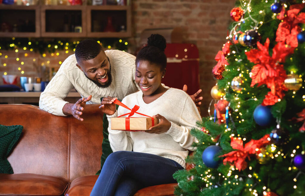Podekscytowana czarna żona rozpakowuje prezent świąteczny od męża - Zdjęcie, obraz