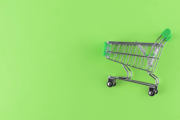 empty green small shopping cart on green background. Copy space, free place for text. - Photo, Image