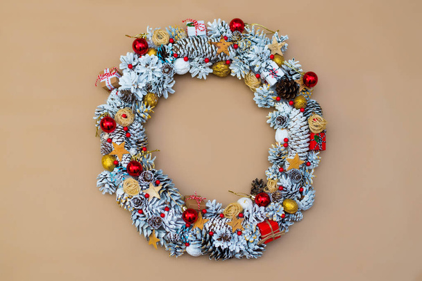 vrchní pohled na ručně vyráběné vánoční věnec s kornouty a červené hračky a dekorativní bobule na řemeslném pozadí - Fotografie, Obrázek