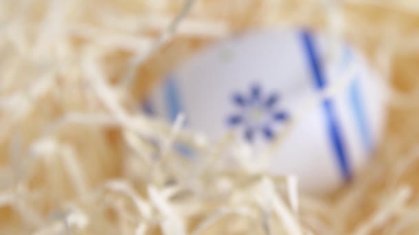 Nahaufnahme Ziehen eines blau-weiß dekorierten Ostereiers aus Stroh - Filmmaterial, Video