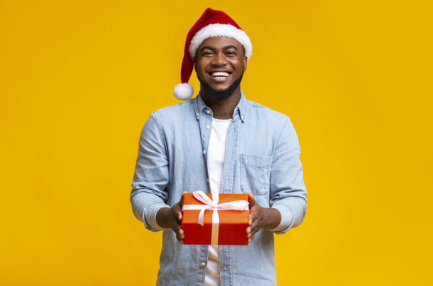 Fešák černošky chlap v červené Santa klobouk drží dárková krabice - Fotografie, Obrázek