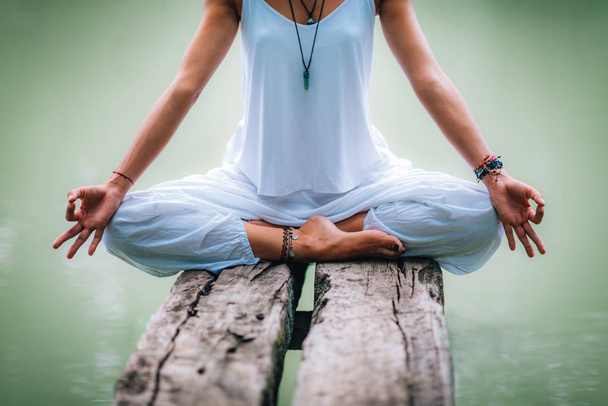 Hermosa joven haciendo ejercicio de yoga junto al lago. Sentado en posición de loto
 - Foto, imagen