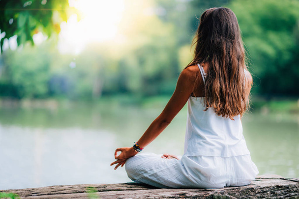 Mulher fazendo ioga junto ao lago, sentada em pose de lótus com os dedos na posição de mudra
. - Foto, Imagem