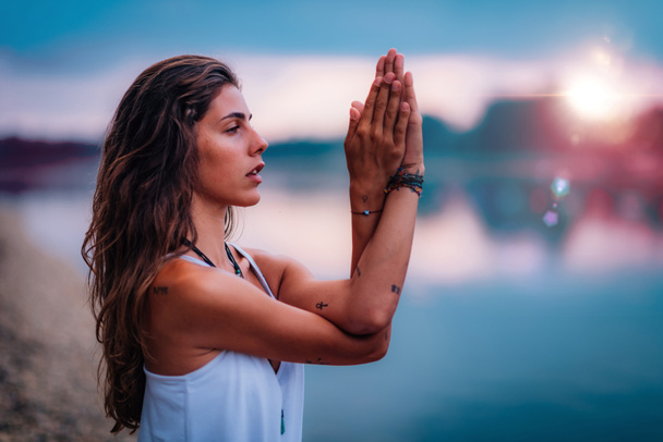 Een jonge vrouw mediteert. Zittend in lotushouding met handen in gebedspositie. - Foto, afbeelding