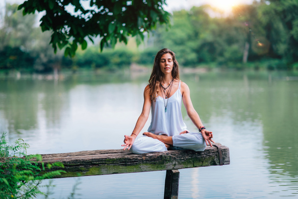 Mujer haciendo yoga junto al lago. Sentado en posición de loto en un muelle de madera
. - Foto, Imagen