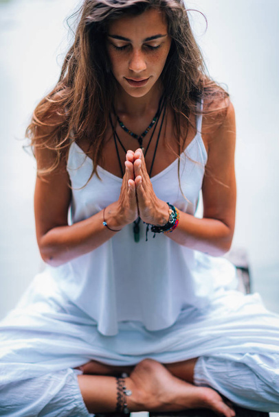 A fiatal nő meditál, jógázik a természetben. Ül lótuszban pózol kezekkel imádkozó pozícióban. - Fotó, kép