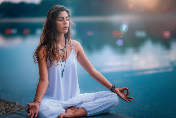 Mujer haciendo yoga junto al lago, sentada en pose de loto con los dedos en posición de mudra
. - Foto, Imagen