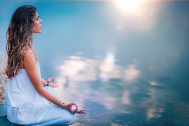 Hermosa joven haciendo ejercicio de yoga junto al lago. Sentado en posición de loto
 - Foto, Imagen