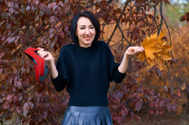 Mooie elegante vrouw die plezier hebben en poseren met boeket van gele bladeren en rode schoenen in de herfst stadspark - Foto, afbeelding