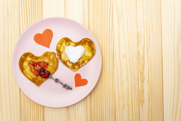 Naleśniki w kształcie serca na romantyczne śniadanie z dżemem truskawkowym, srebrną łyżką i papierowymi sercami. Koncepcja shrovetide (karnawał). Na drewnianym tle, widok z góry - Zdjęcie, obraz