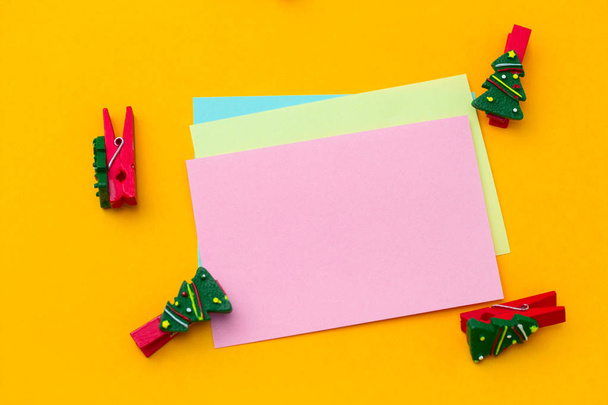 top view festive christmas clothespin and empty paper sheets with free space for text  on a vibrant yellow background - Foto, Imagem