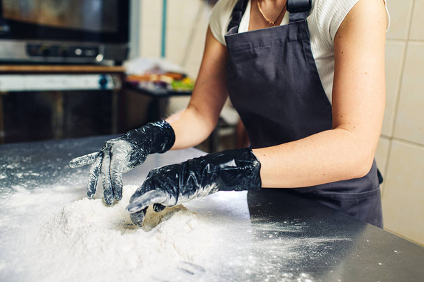 les mains du boulanger en gants noirs pétrissent la pâte
. - Photo, image