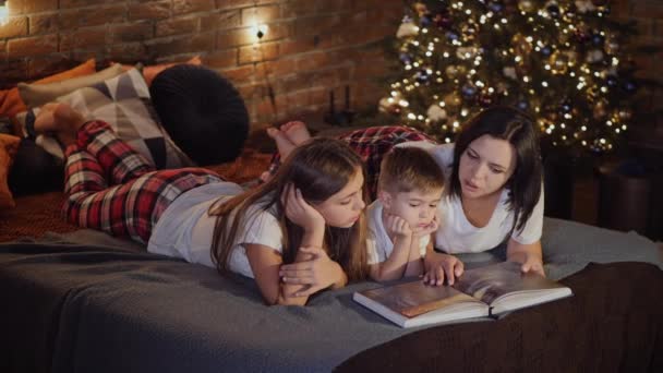 Mutter liest Kindern im Schlafzimmer ein Buch vor - Filmmaterial, Video