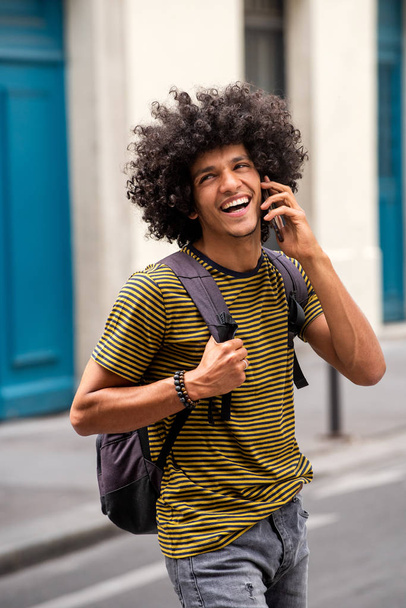 Çantasıyla yürüyen ve cep telefonuyla konuşan gülümseyen genç adamın portresi. - Fotoğraf, Görsel