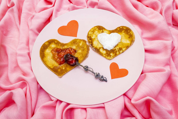 Naleśniki w kształcie serca na romantyczne śniadanie z dżemem truskawkowym, srebrną łyżką i papierowymi sercami. Koncepcja shrovetide (karnawał). Na różowym tle płótna tkaniny - Zdjęcie, obraz