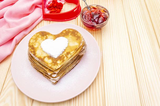 Naleśniki w kształcie serca na romantyczne śniadanie z dżemem truskawkowym i formą serca. Koncepcja shrovetide (karnawał). Na drewnianym tle z różowym płótnem - Zdjęcie, obraz