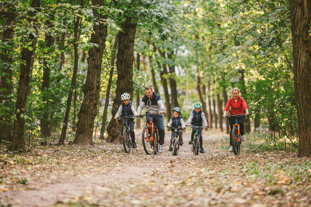rodziców i dzieci jeżdżących po leśnym szlaku. Młoda rodzina jeździ na rowerze w jesiennym parku. Rodzinny rower górski po lesie. Rodziny tematyczne aktywny sport rekreacji na świeżym powietrzu. Jazda na rowerze rodzinnym przez jesienny las - Zdjęcie, obraz