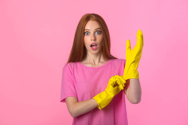 beautiful young woman with red hair in yellow rubber gloves on a pink background - Foto, imagen