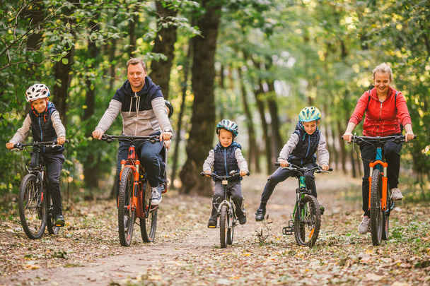 батьки та діти катаються на велосипеді по лісовій стежці. Молода сім'я в теплому одязі їздить на велосипеді в осінньому парку. Сімейні гірські велосипеди на лісі. Тематичні сімейні активні види спорту відпочинок на відкритому повітрі
. - Фото, зображення