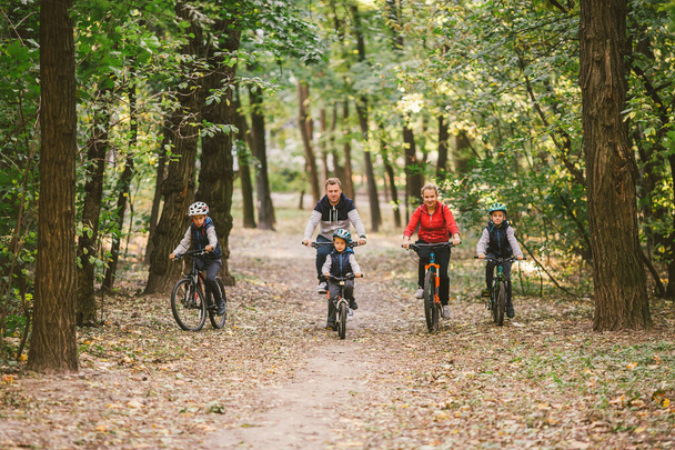 Батьки і діти їздять на велосипеді по лісовій стежці. Молода сім'я їздить на велосипеді в осінньому парку. Сімейні гірські велосипеди в лісі. Сім'я Тем активно займається спортом на відкритому повітрі. Сімейні велосипеди в осінньому лісі - Фото, зображення