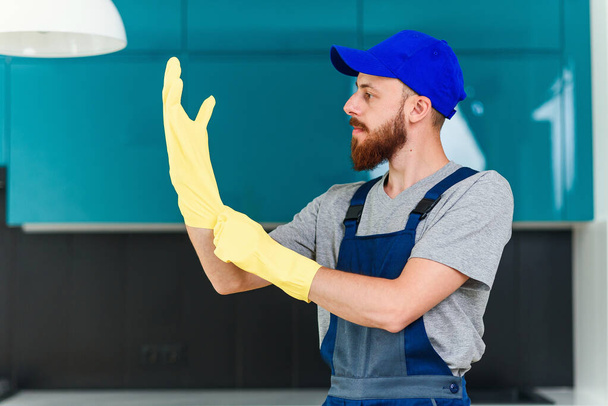 Attractive guy with well-groomed beard from cleaning service wearing protective rubber gloves to clean the domestic cuisine - Foto, afbeelding