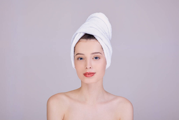 A girl with a towel on her hair looks straight and smiles. - Foto, afbeelding