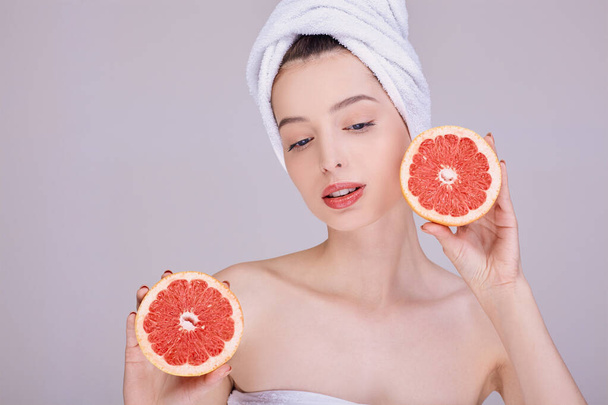 Girl with clean skin, half-naked, in a towel on her head, holds in her hands a fresh grapefruit. - Photo, Image