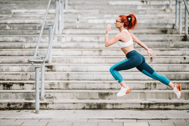 Portrait of sportswoman with fit body jumping and running on stairs background. Woman doing hardcore cardio training - Fotó, kép