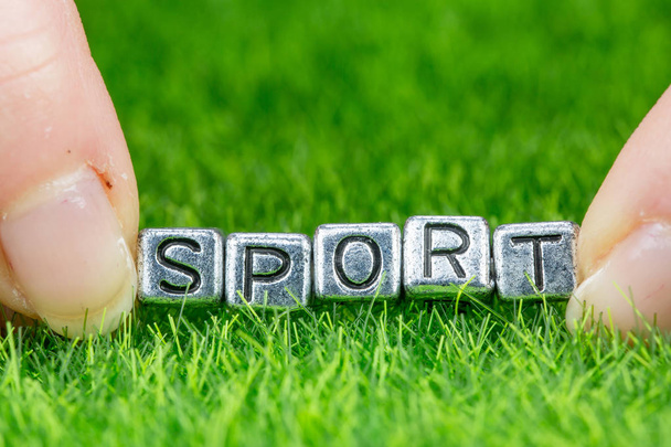 Word SPORT written in metal letters laid on grass and held between the fingers of a woman. Concept of activity background - Photo, image