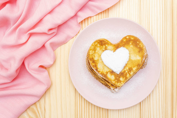 Naleśniki w kształcie serca na romantyczne śniadanie. Koncepcja shrovetide (karnawał). Na drewnianym tle z różowym płótnem, widok z góry - Zdjęcie, obraz