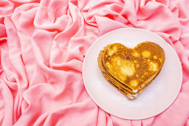 Aşk kahvaltısı için pembe tabakta kalp şeklinde gözleme. Shrovetide (karnaval) konsepti. Pembe kumaş arkaplanda - Fotoğraf, Görsel