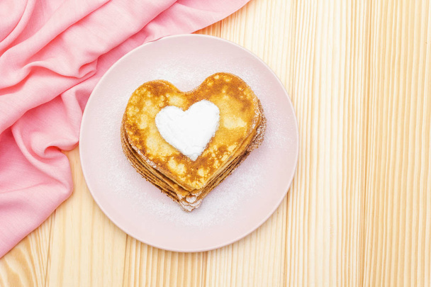 Romantik kahvaltı için kalp şeklinde gözleme. Shrovetide (karnaval) konsepti. Ahşap arka planda pembe keten kumaşlar, üst manzara - Fotoğraf, Görsel