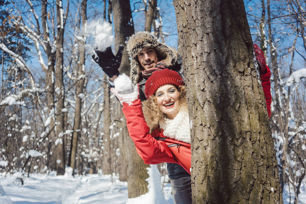 Nainen ja mies talvella heittää lumipallo piilossa puun takana
 - Valokuva, kuva