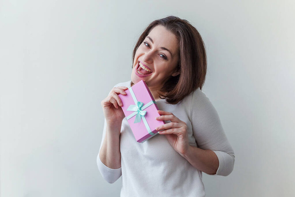 Young positive woman holding small pink gift box isolated on white background. Preparation for holiday. Girl looking happy and excited - Fotoğraf, Görsel