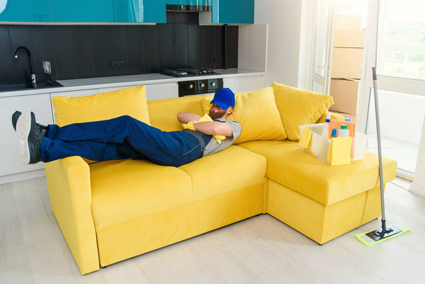 Tired man in special uniform sleeps on couch after cleaning cuisine. - Foto, afbeelding