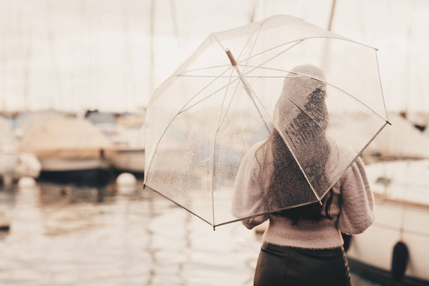 Outdoor portrait of young woman under the rain, holding umbrella, looking far away, back view, retro styled image - Photo, Image