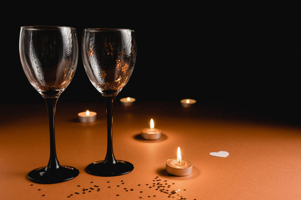 Holiday background. Two clinking wine glasses, candle, confetti on orange and black background. Minimal style and valentines day concept. Flat lay, copy space - Fotoğraf, Görsel